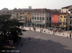 A Piazza Bra é maior praça de Verona e seu nome é originário do termo braida que, por sua vez, deriva do alemão breit, ou seja, largo, amplo, um vasto espaço. E de fato é uma praça grande e abriga diversos palácios, casas e monumentos de épocas muito diferentes entre si, desde a Antigüidade Romana até o século XIX. À esquerda da praça, para quem chega dos Portoni della Bra, vemos o Teatro Filarmonico, cuja construção iniciou-se em 1716 e concluído somente em 1729, sendo destruído quase completamente durante a II Grande Guerra e reconstruído de acordo com o projeto inicial. Do outro lado da rua, vemos fileiras de casas coloridas com toldos verdes que abrigam restaurantes e bares de público mais seleto, ao centro, uma grande árvore e um pequeno chafariz, ao fundo, a imponente Arena, um dos símbolos da cidade e herança dos nossos ancestrais romanos, à direita, o edifício do Município de Verona e o Palazzo della Gran Guardia, construído no início de 1610 e concluído na metade do século XVIII. <br><br/> Palavras-chave: Itália, arquitetura, Verona, arte renascentista.